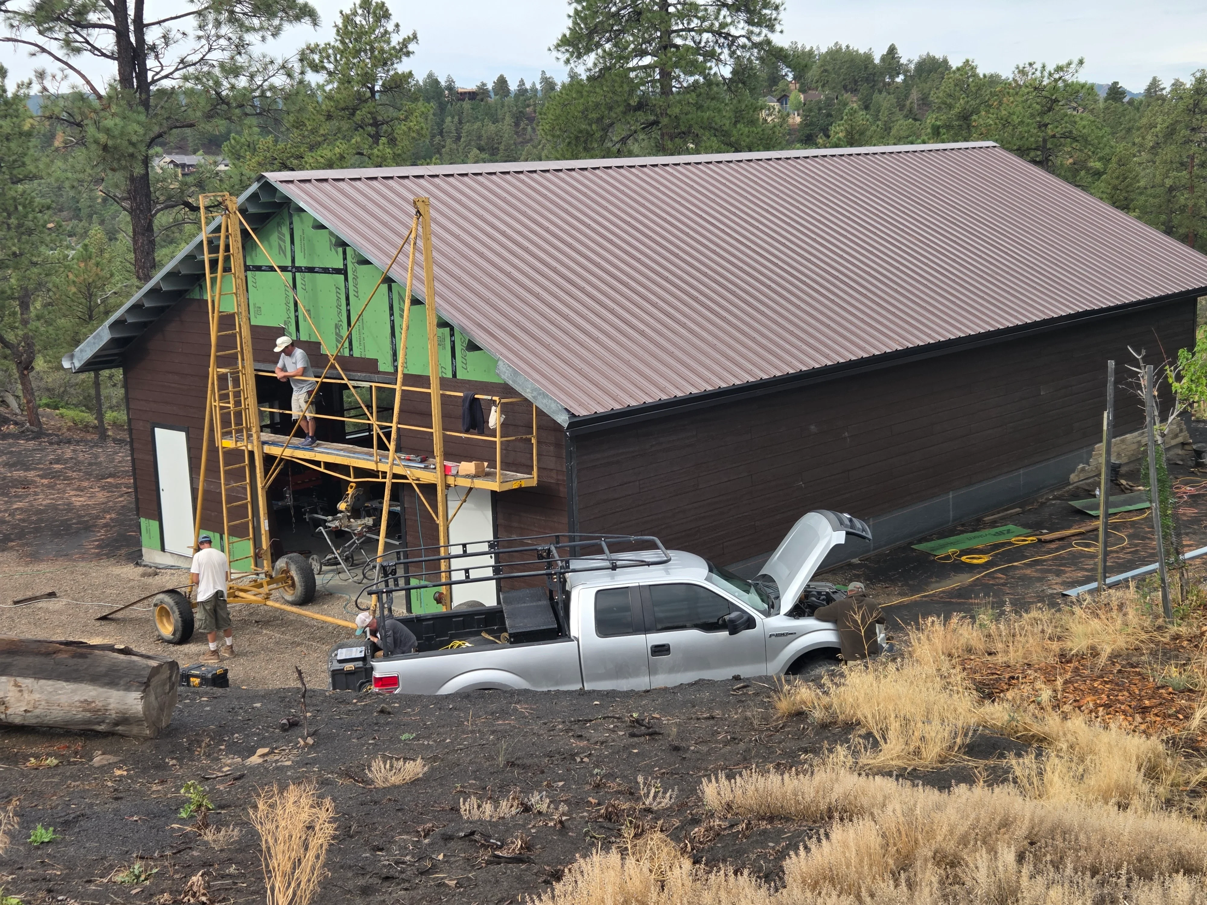 Standing seam metal roof installation on residential building with dark wood siding and elevated work platform