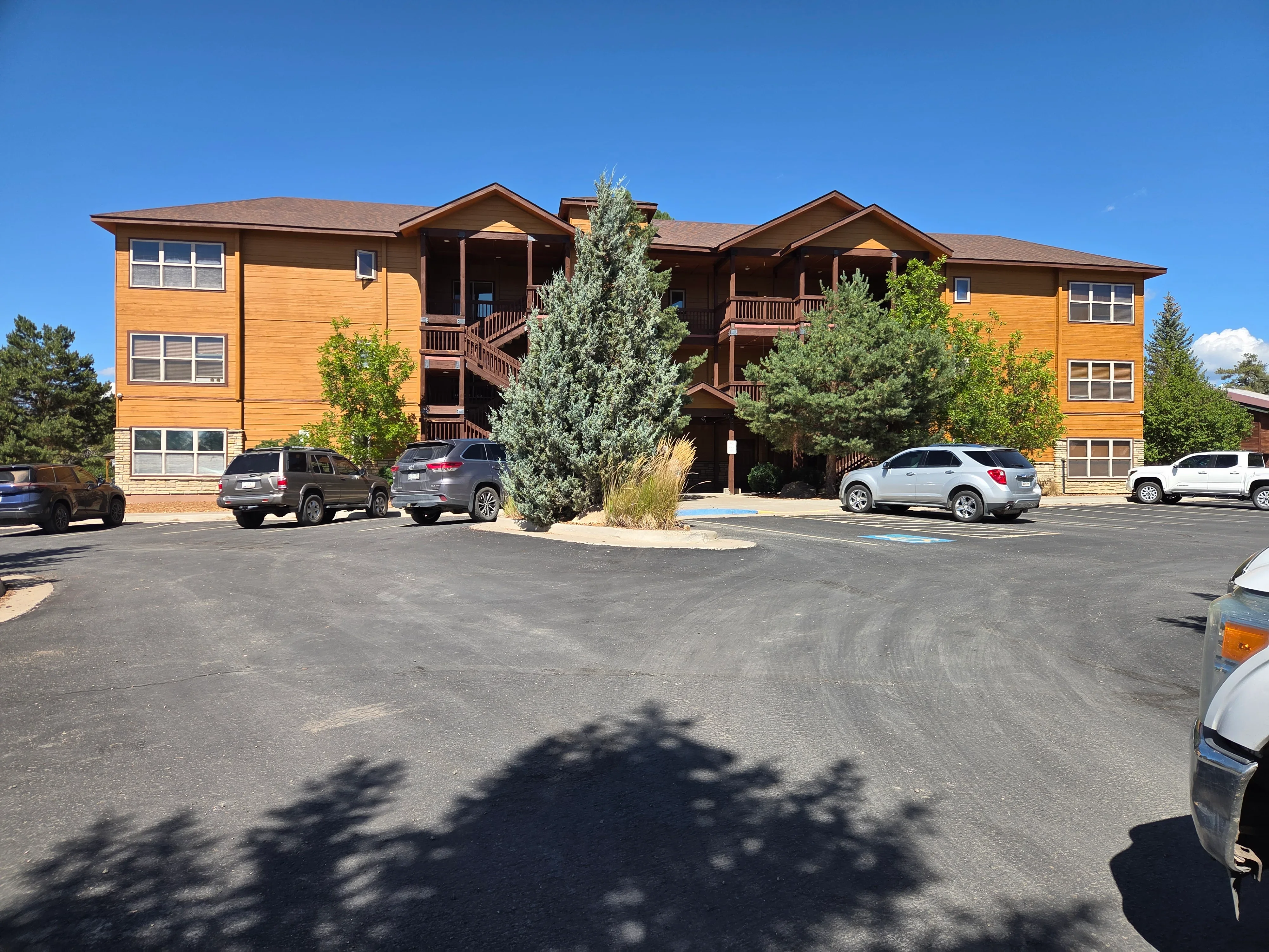 Three-story residential building with wood siding, multiple balconies, and asphalt parking area