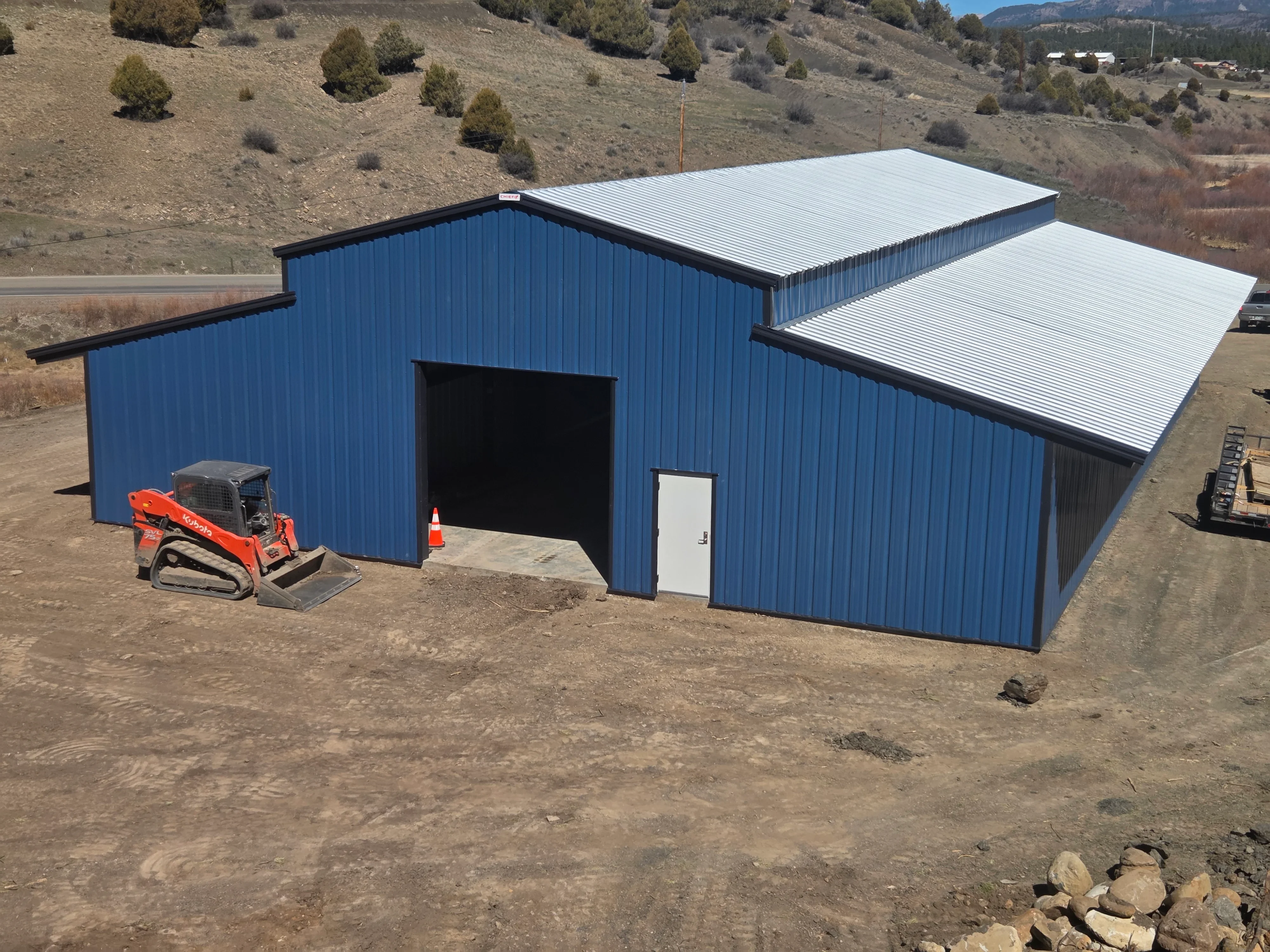 Blue corrugated metal storage building with white metal roof canopies and large bay door