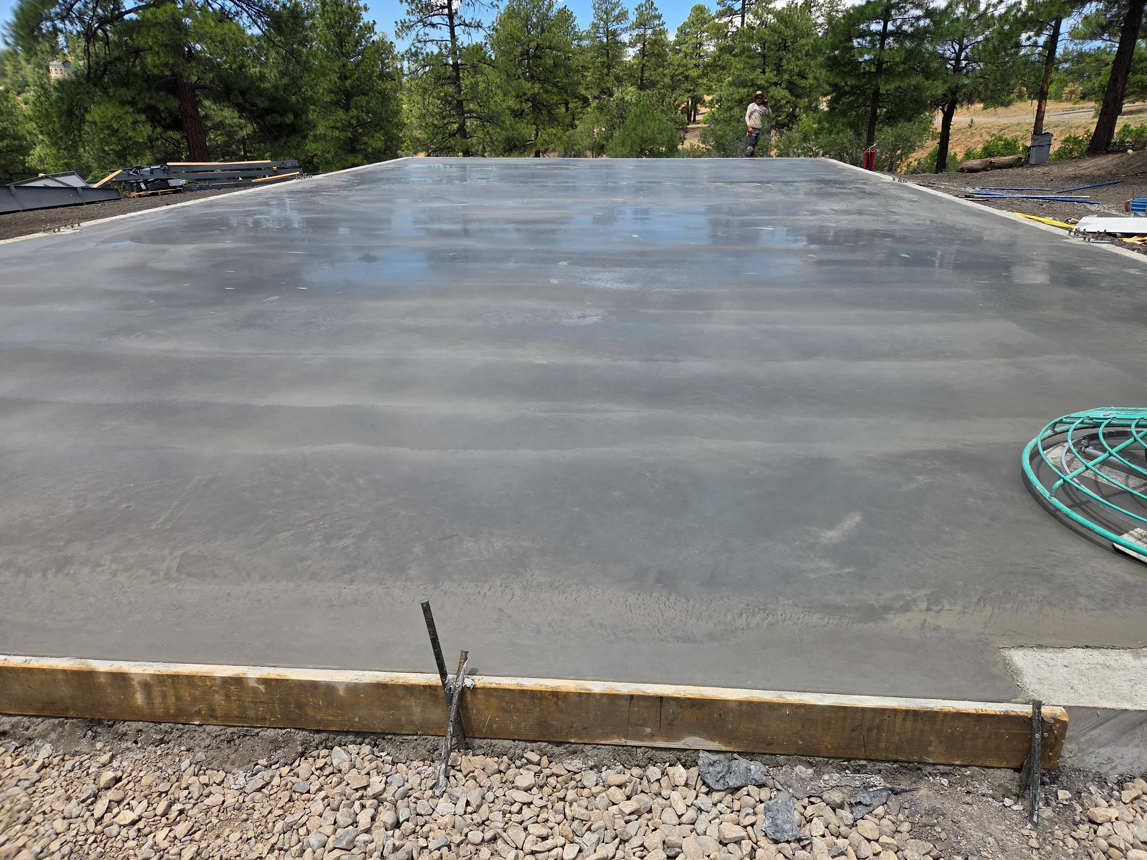 Finished concrete foundation slab with wooden forms and gravel base in forested setting
